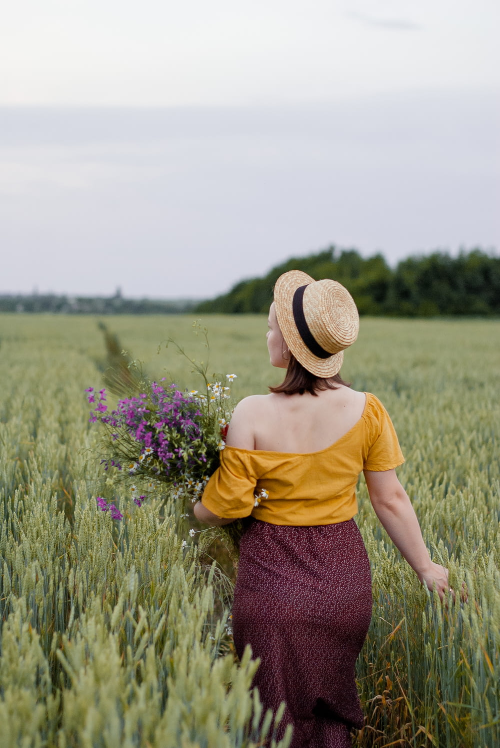 woman in yellow shirt and purple skirt wearing brown straw hat standing on green grass field