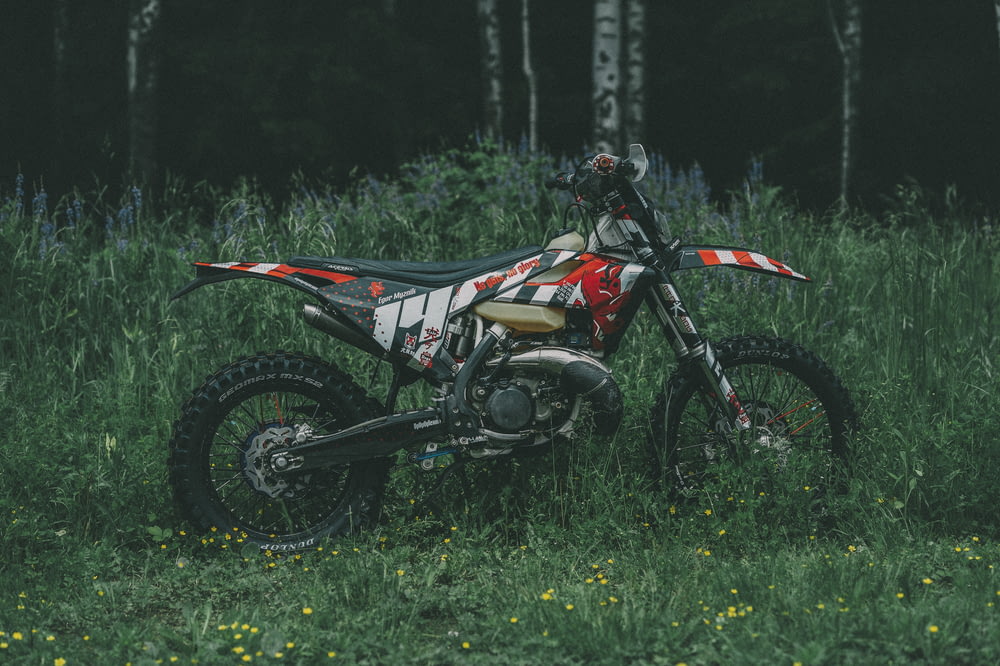 moto de cross de motocross roja y negra en el campo de hierba verde durante el día