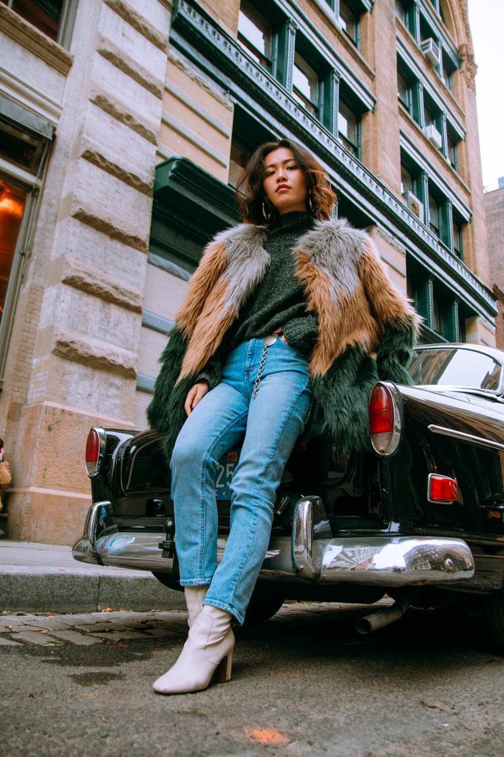 woman in brown fur coat and blue denim jeans standing beside black car during daytime