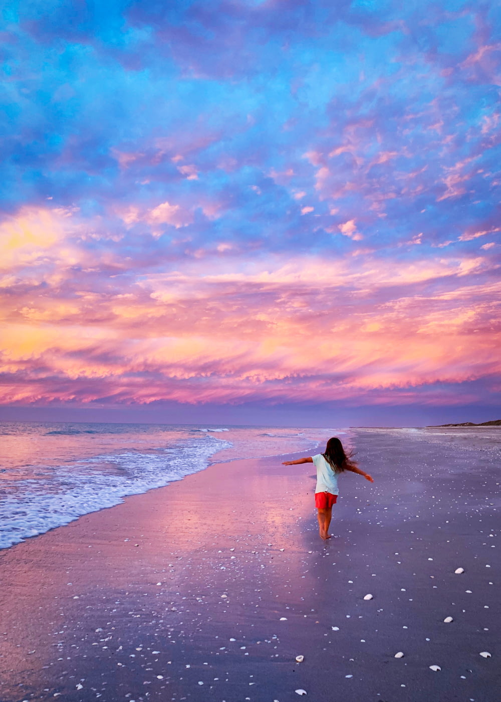 donna in vestito bianco che cammina sulla spiaggia durante il tramonto
