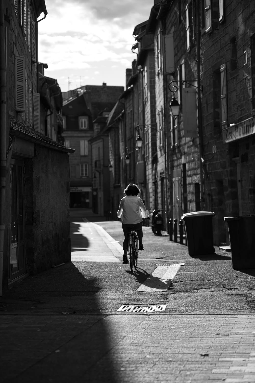 man in white shirt riding bicycle on street in grayscale photography