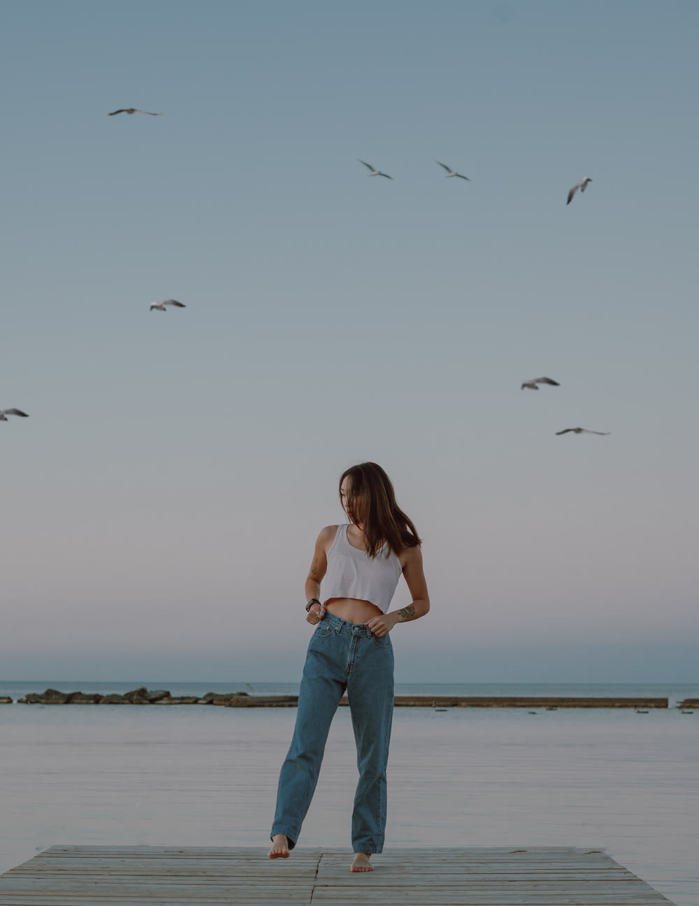 woman in blue denim jeans standing on seashore during daytime