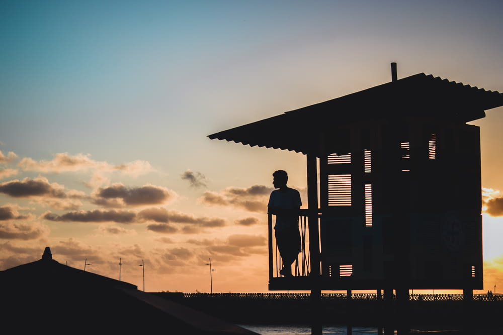 silhouette of man standing on wooden dock during sunset