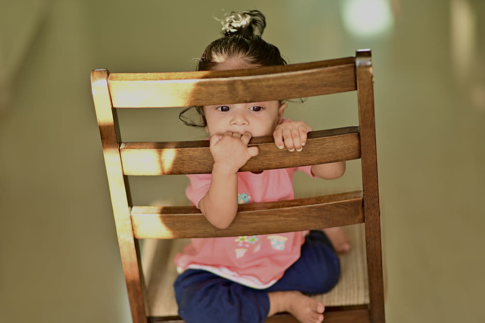 girl in blue shirt lying on brown wooden chair