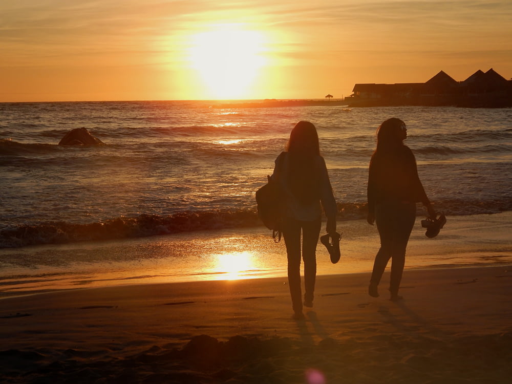 silhouette of 2 women walking on beach during sunset