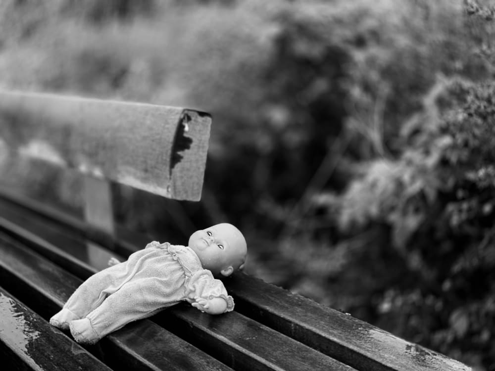 Photo en niveaux de gris de poupée de bébé sur un banc en bois