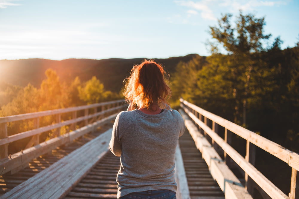 a woman standing on a bridge looking at the sun