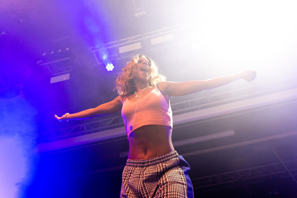 woman in white sports bra and black and white plaid skirt standing on stage