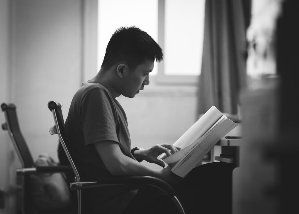 Foto en escala de grises de un hombre leyendo un libro