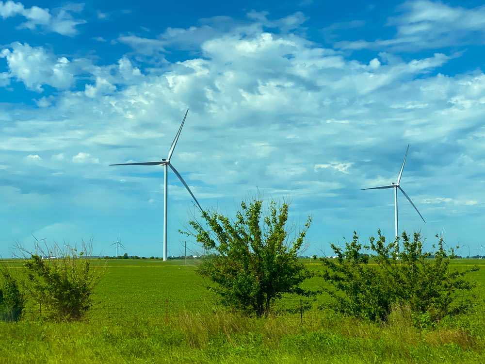 낮 동안 파란색과 흰색 흐린 하늘 아래 푸른 잔디밭의 풍력 터빈