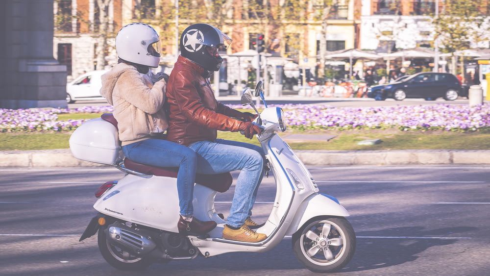woman in brown jacket and blue denim jeans sitting on white motor scooter during daytime