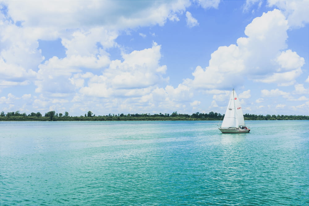 white sailboat on sea under blue sky and white clouds during daytime