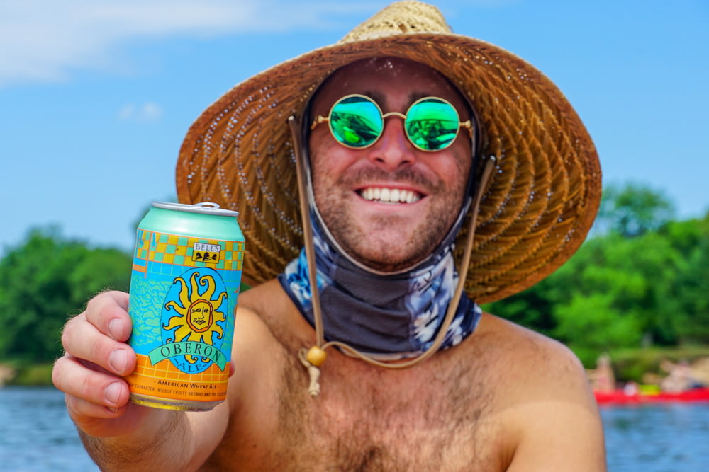 topless man wearing brown straw hat holding yellow and blue can