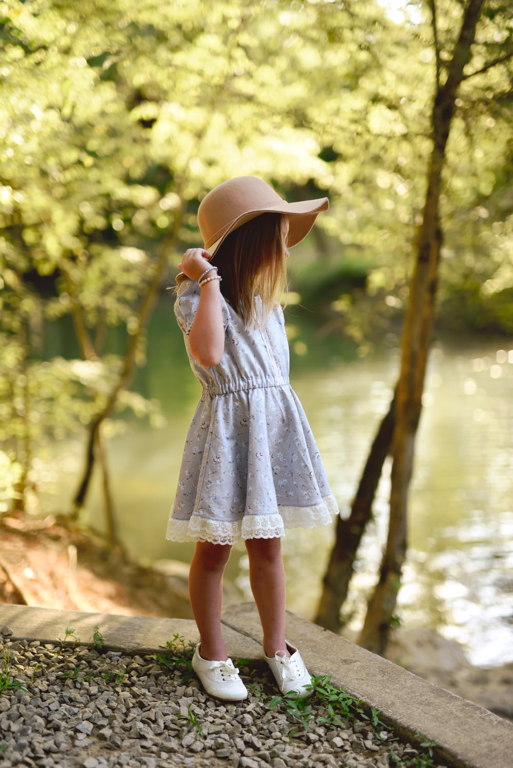 灰色のドレスを着た女性が茶色の日よけ帽をかぶって、昼間、水辺に立っている