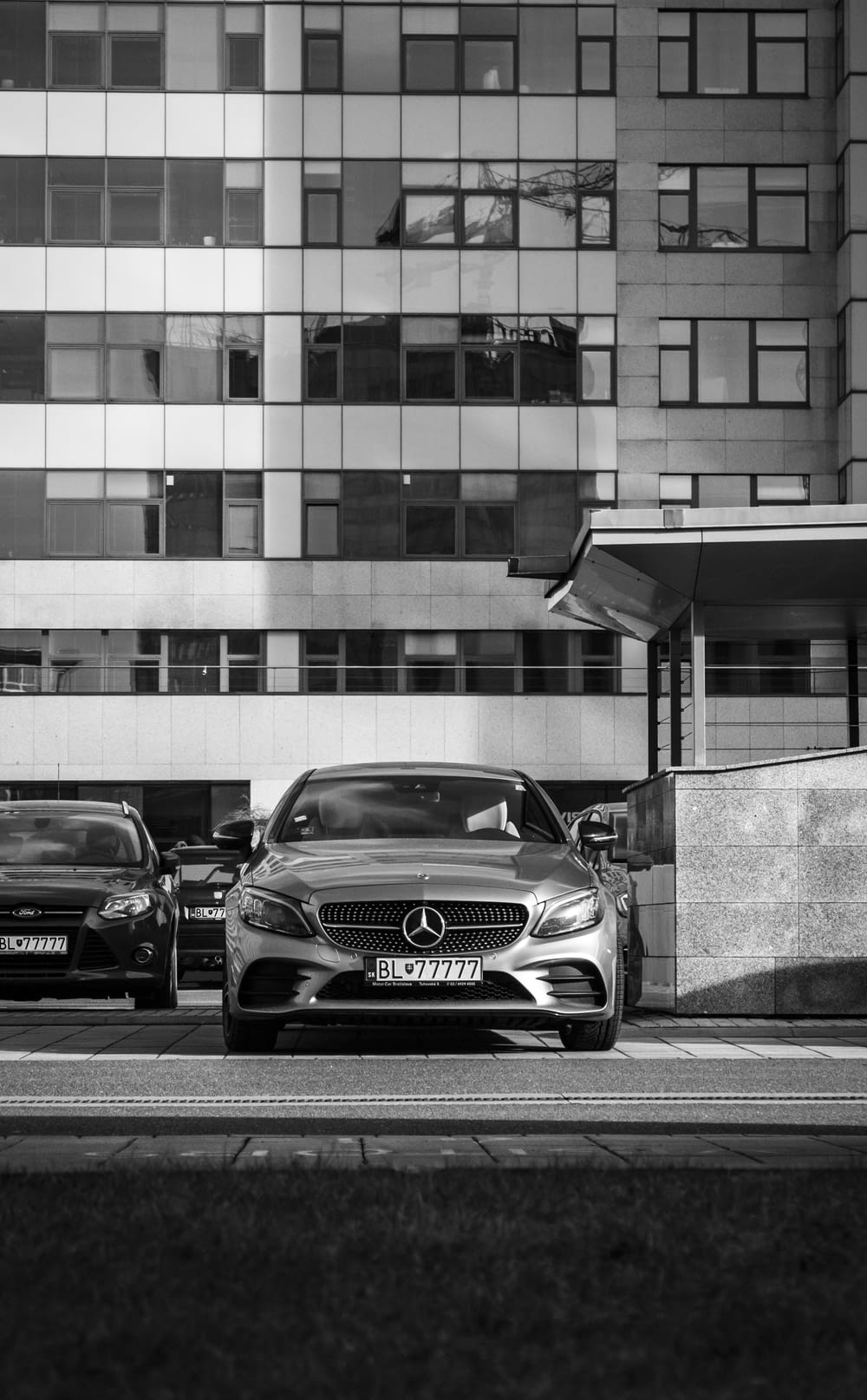 grayscale photo of mercedes benz coupe parked beside building