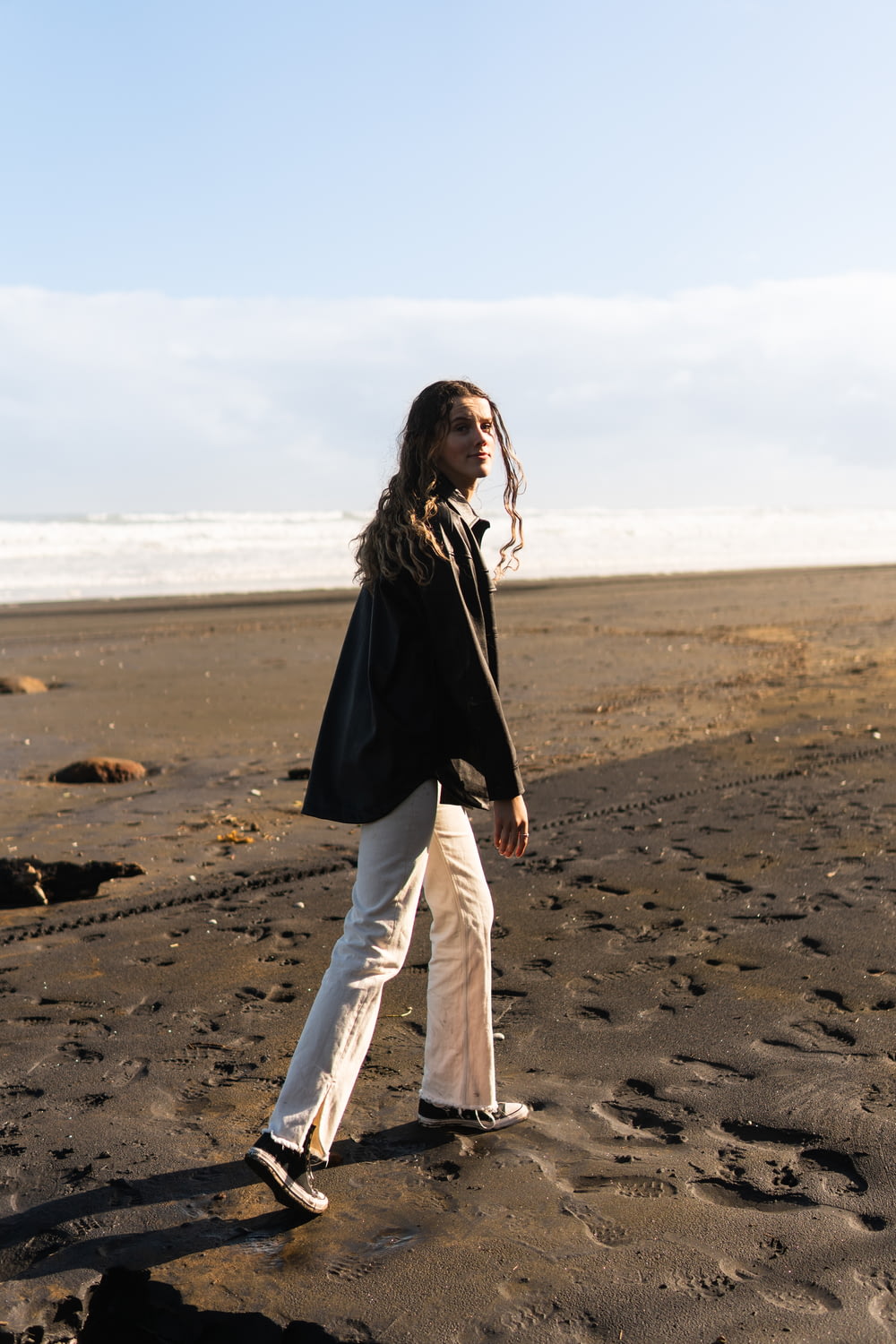 woman in black long sleeve shirt and white pants standing on brown sand during daytime