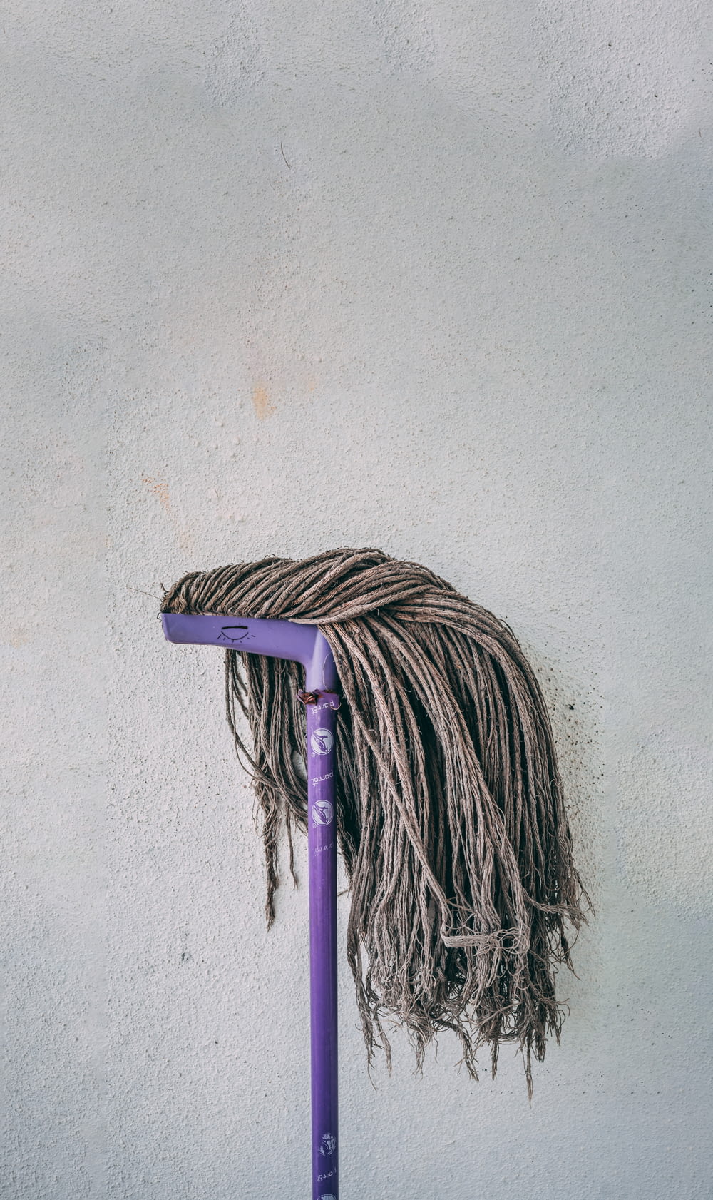 purple and white mop leaning on white wall