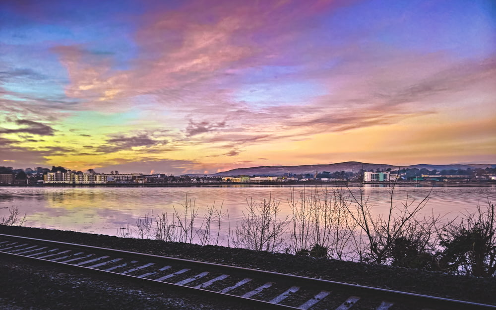 black train rail near body of water during sunset