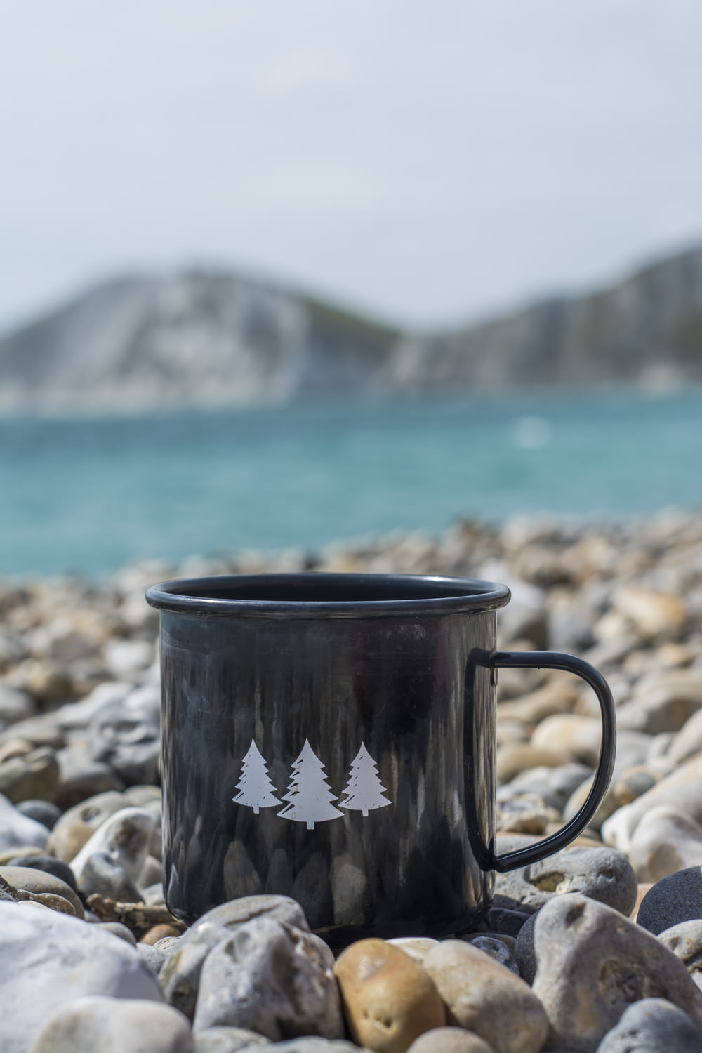 black and white ceramic mug on rocky shore during daytime
