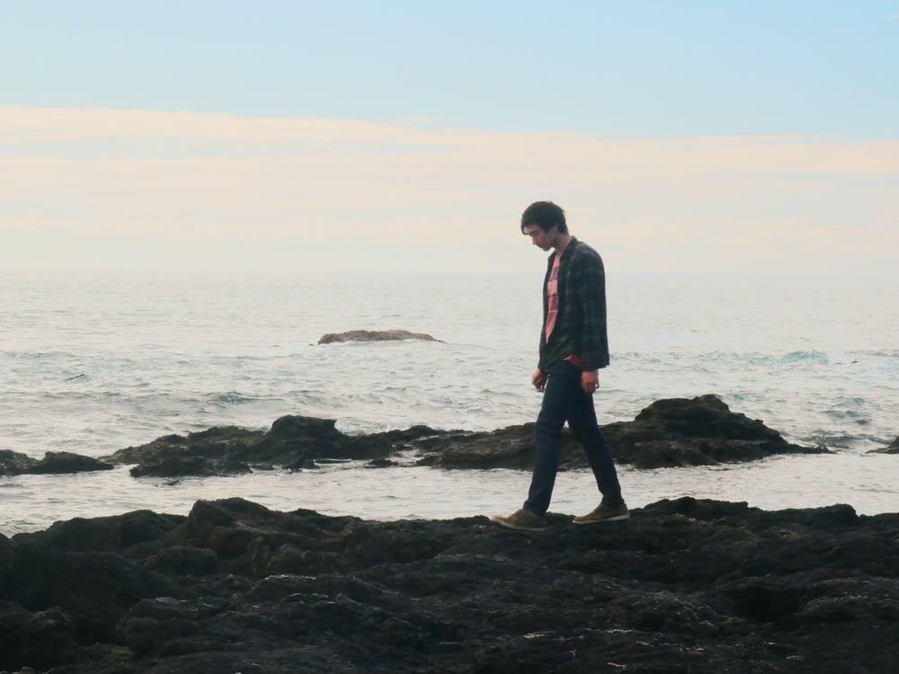 man in red jacket standing on black rock near sea during daytime