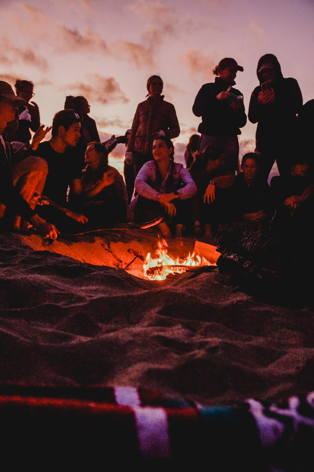 persone sedute sulla sabbia marrone vicino al falò durante la notte
