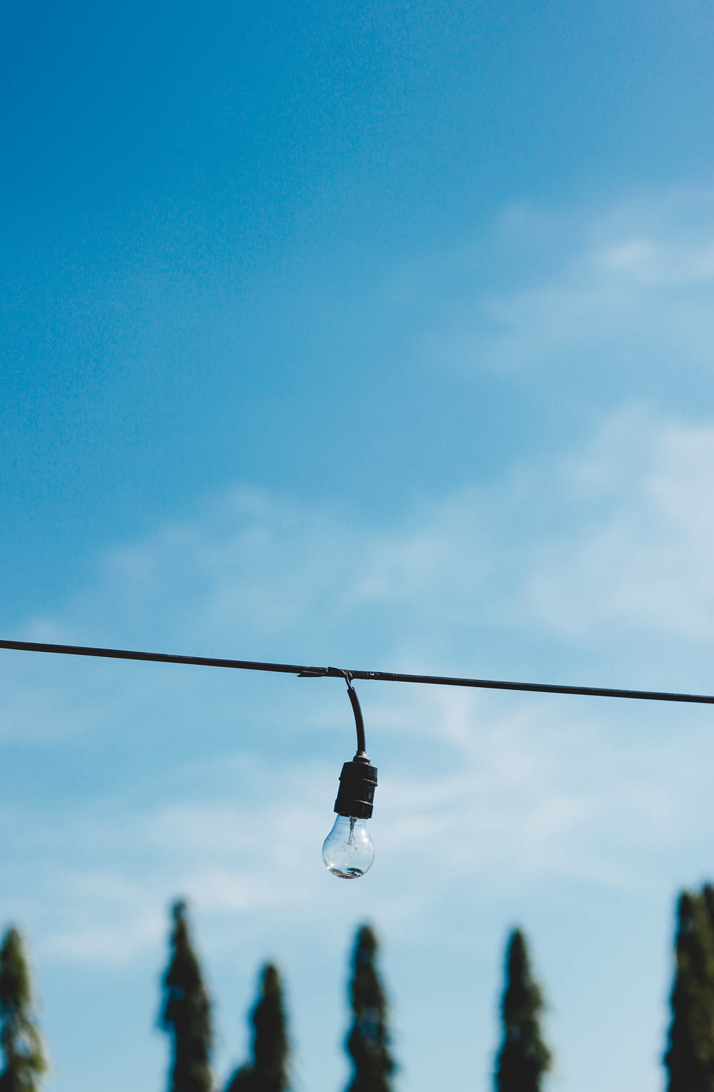 white light bulb on black electric wire under blue sky during daytime