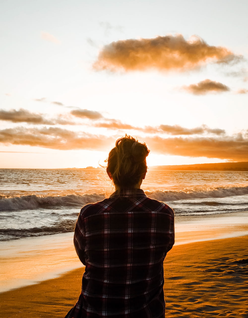 woman in black and white plaid dress shirt standing on seashore during sunset