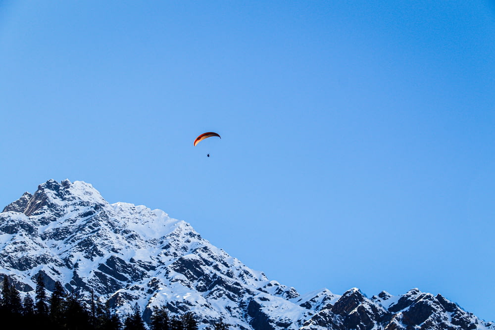 person in orange parachute over snow covered mountain during daytime