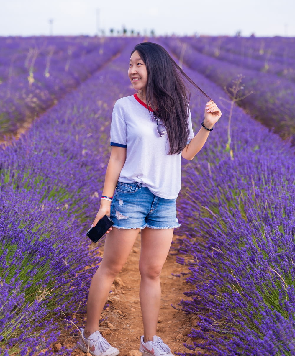 woman in white t-shirt and blue denim shorts standing on purple flower field during daytime