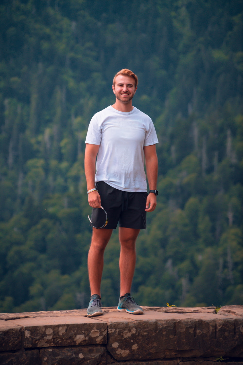 homem em camiseta branca do pescoço da tripulação e shorts pretos em pé na montanha durante o dia