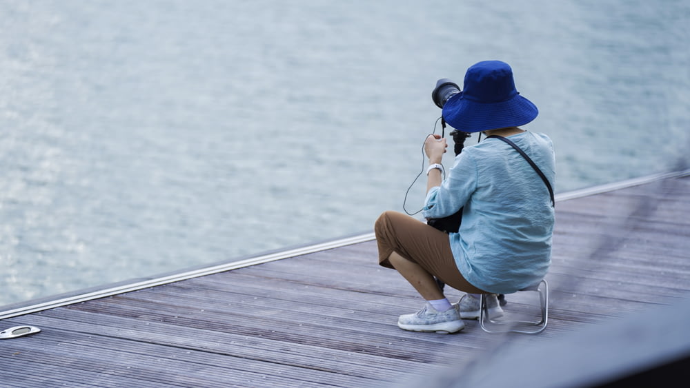 woman in blue shirt and brown shorts sitting on dock