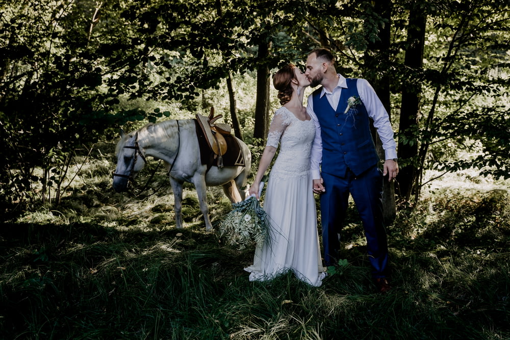 낮 동안 푸른 잔디밭에서 갈색 말 옆에 서 있는 남자와 여자