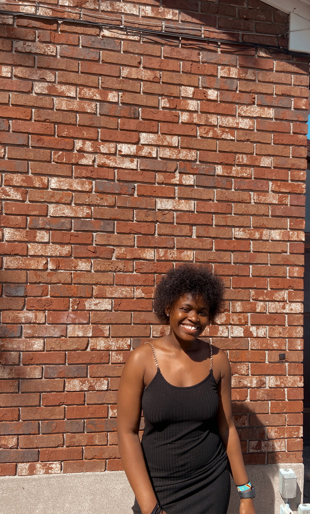 woman in black tank top standing beside brick wall