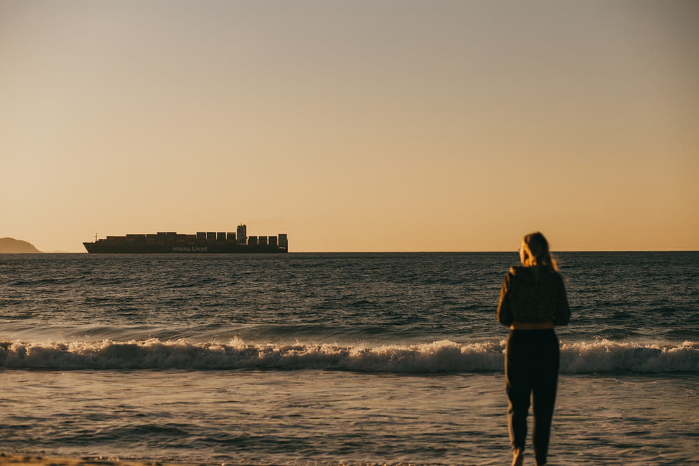 femme en robe noire debout sur le bord de la mer pendant le coucher du soleil