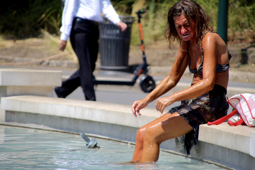 woman in white shirt and black shorts sitting on water fountain during daytime