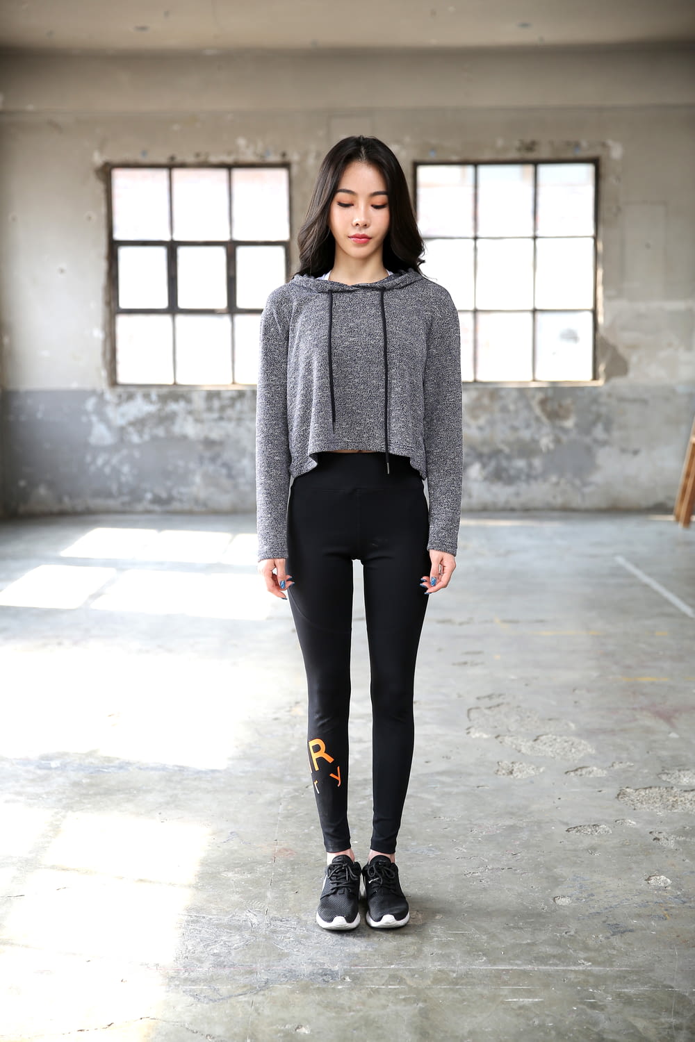 woman in gray sweater and black pants standing on gray concrete floor
