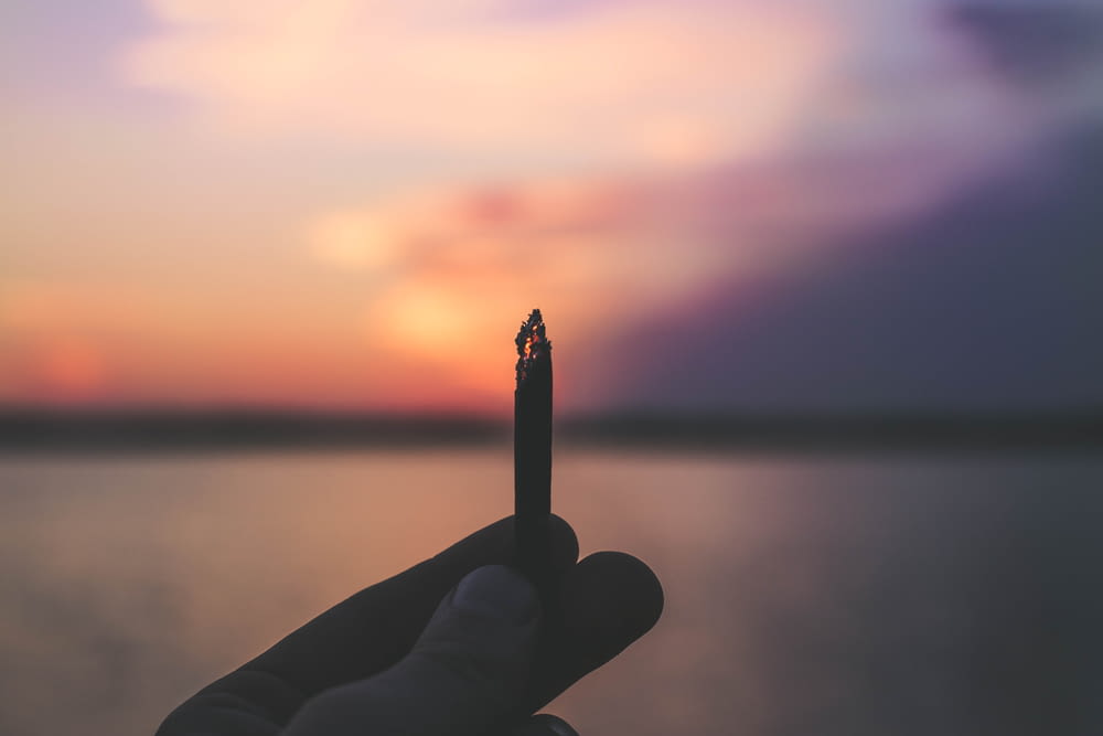 Person, die während des Sonnenuntergangs eine angezündete Zigarettenstange hält