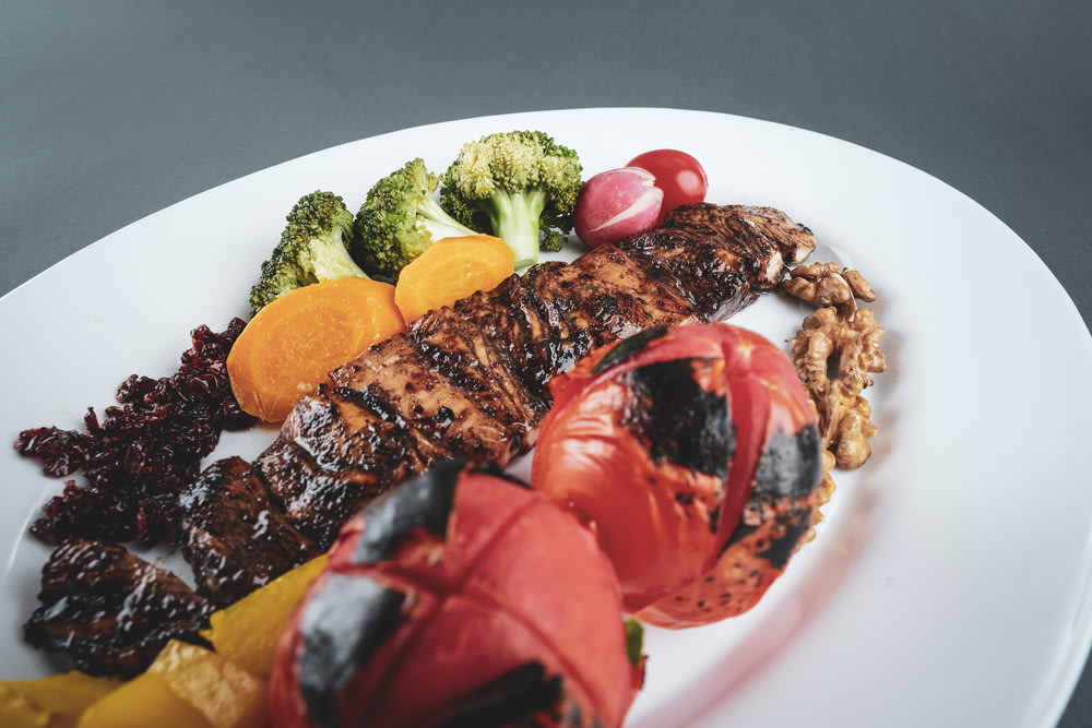 grilled meat with sliced tomato and green vegetable on white ceramic plate