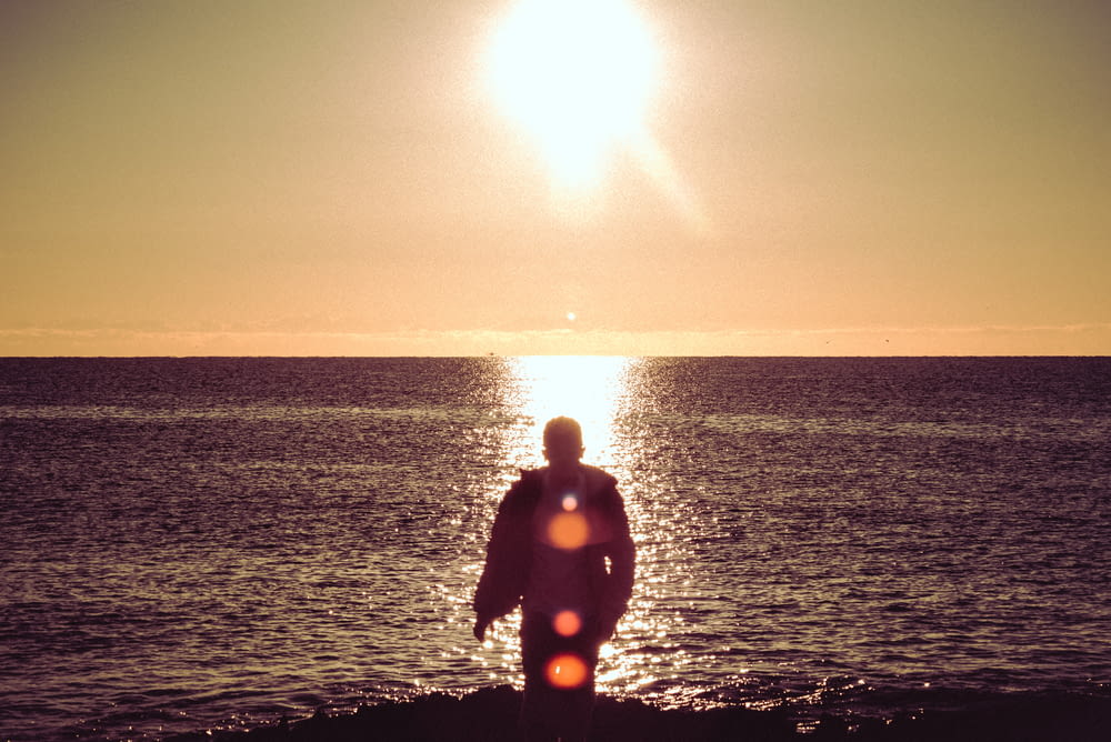 man in black wet suit standing on sea shore during sunset
