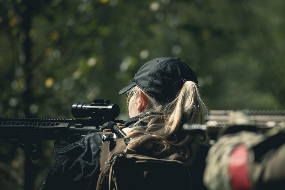mulher na jaqueta preta que segura o rifle preto