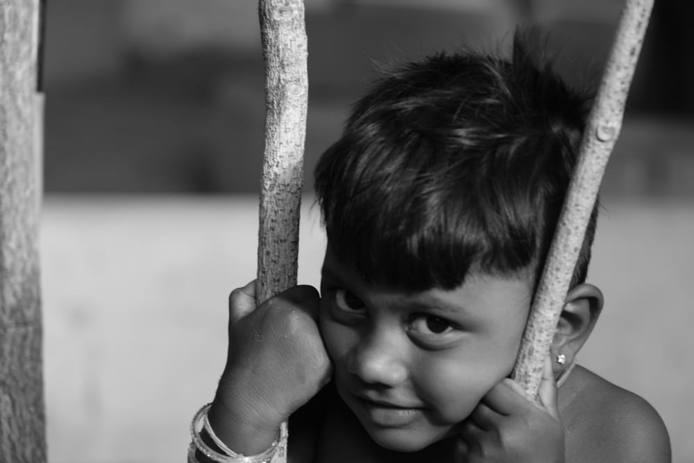 grayscale photo of boy holding on tree branch