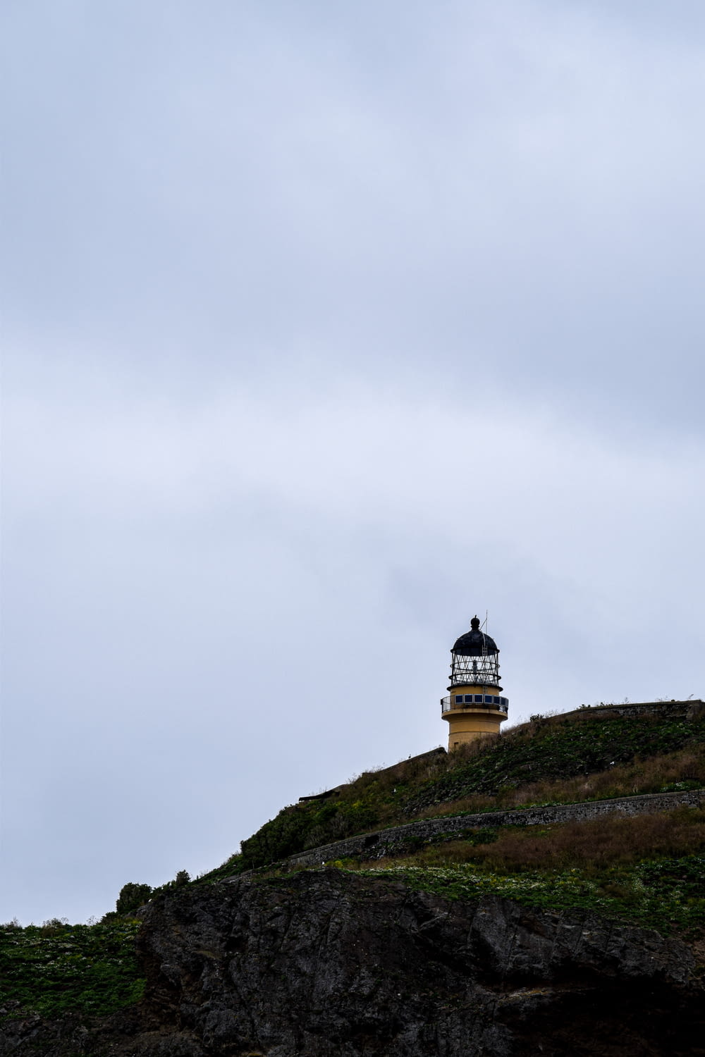 white and black lighthouse on green grass covered hill under white cloudy sky during daytime