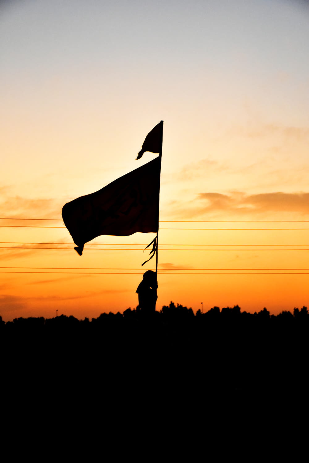 Silhouette eines Mannes, der während des Sonnenuntergangs eine Flagge hält