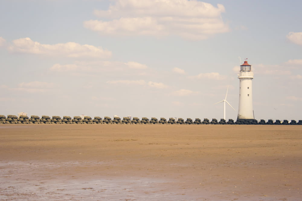 white lighthouse on brown sand near body of water during daytime