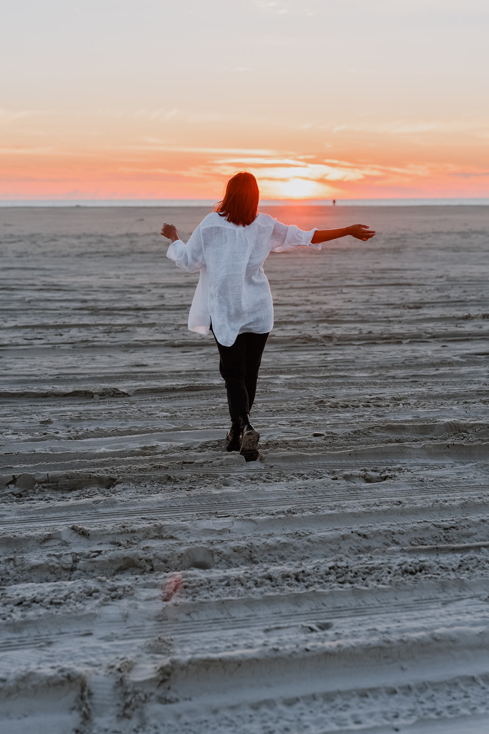 woman in white long sleeve shirt and black pants standing on beach during sunset