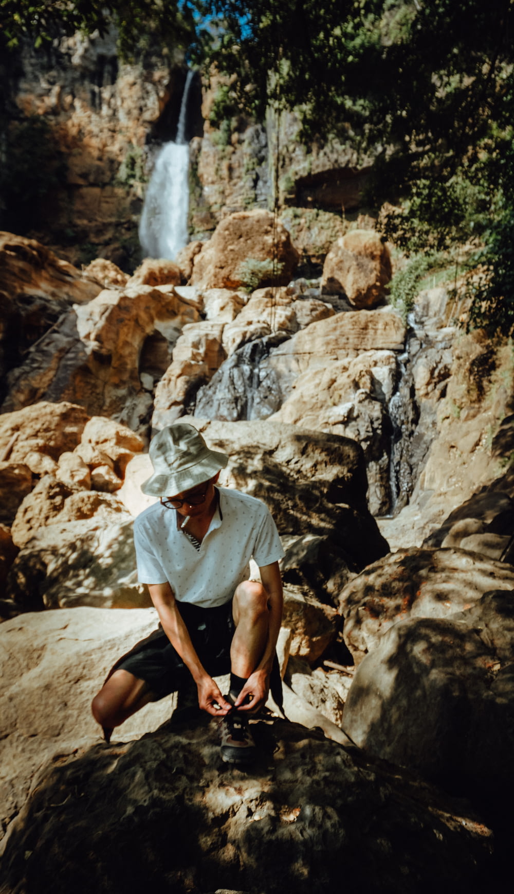 woman in white hijab sitting on brown rock near waterfalls during daytime