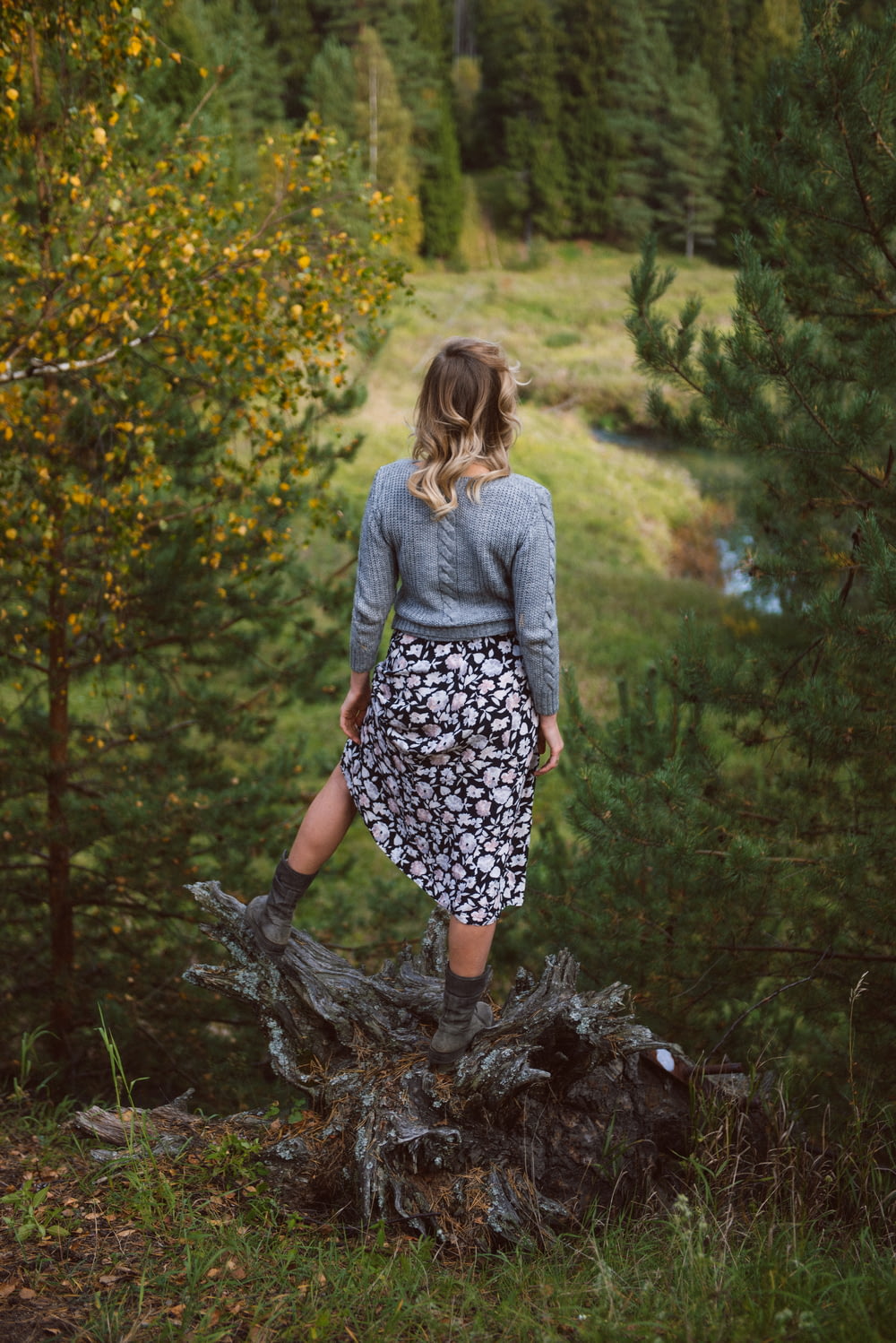 woman in gray long sleeve shirt and black and white floral skirt standing on brown tree