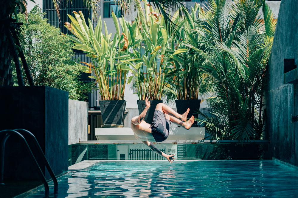 man in black shorts jumping on swimming pool during daytime