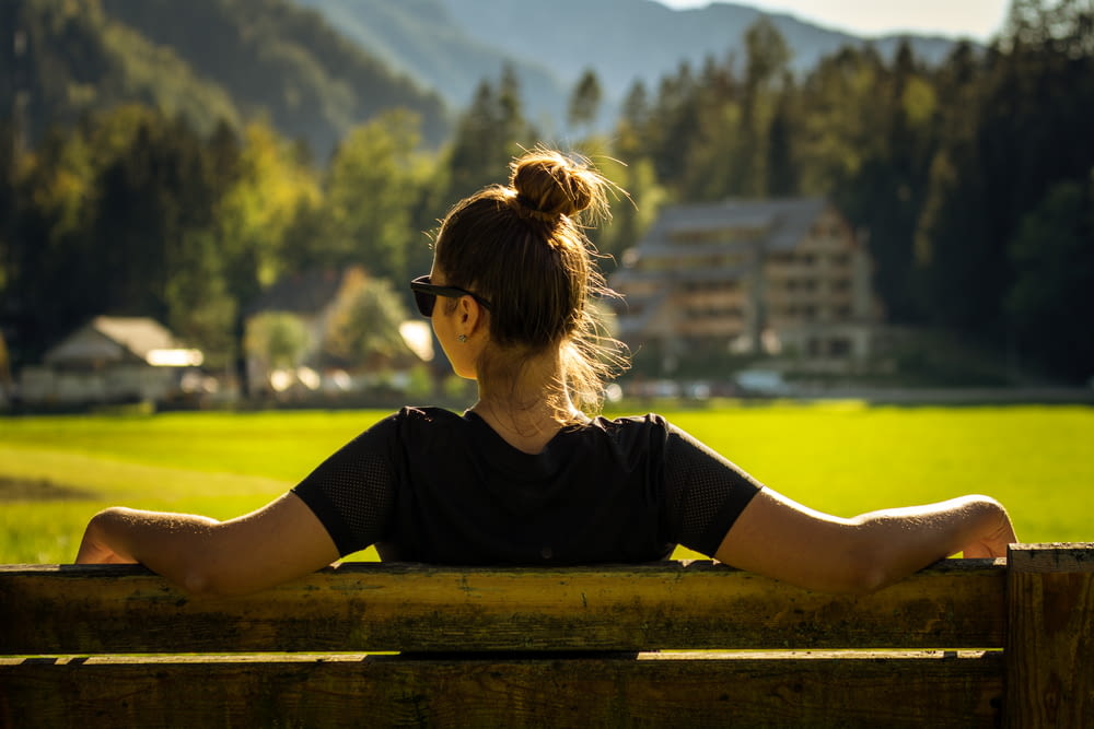 Donna in t-shirt girocollo nera seduta su panca di legno marrone durante il giorno