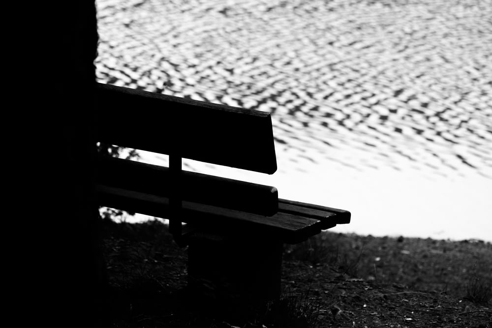 grayscale photo of bench near body of water